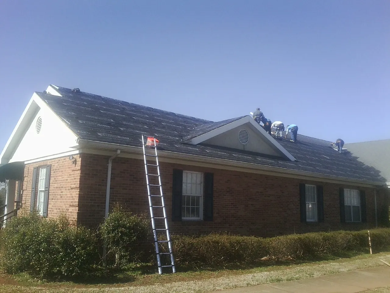 Crew tearing shingles off a brick ranch roof with a ladder set — Emergency Roof Repair work by our crew in Reedley