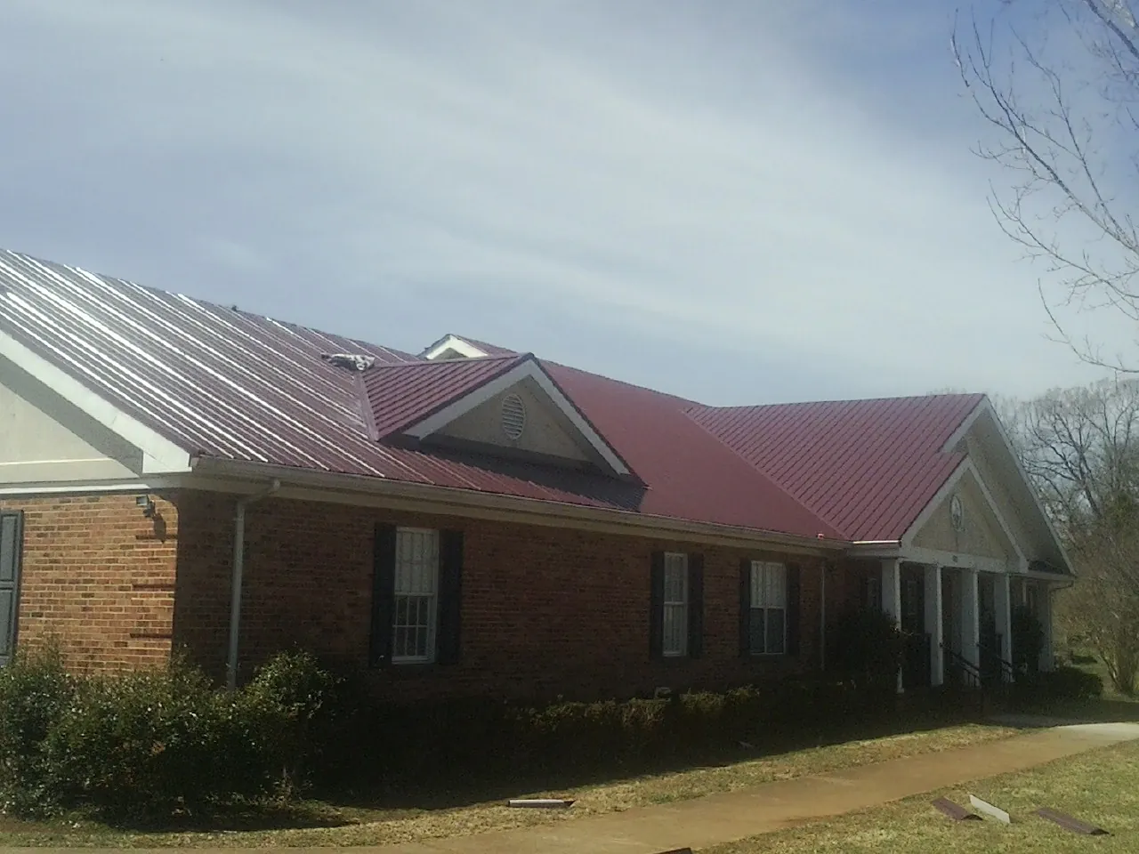 Red metal roof with gabled entries on a long brick building, from a Hail Damage Roof Repair job in Reedley