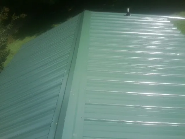 New green metal panels meeting at the ridge of a roof — Flat Roof Repair work by our crew in Reedley