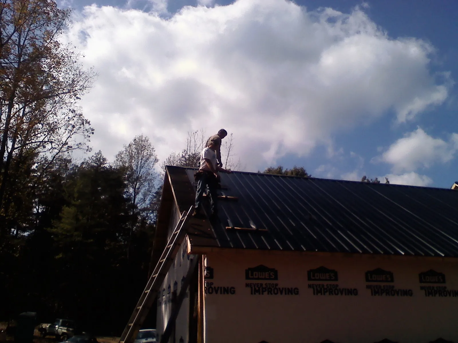 Roofer fastening dark metal panels high against a cloudy sky, from a Roof Inspection job in Reedley